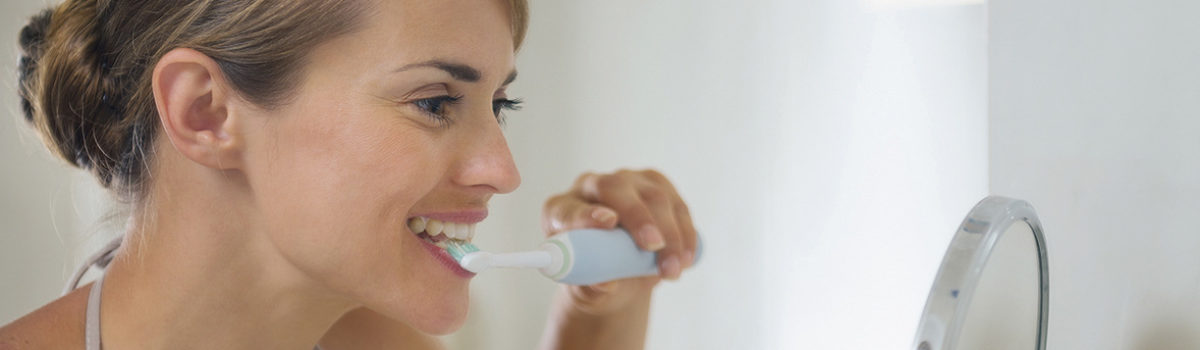 Frau putzt sich Zähne vor dem Speigel